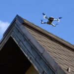 Drone in the air inspecting the roof over the house closeup blue sky background