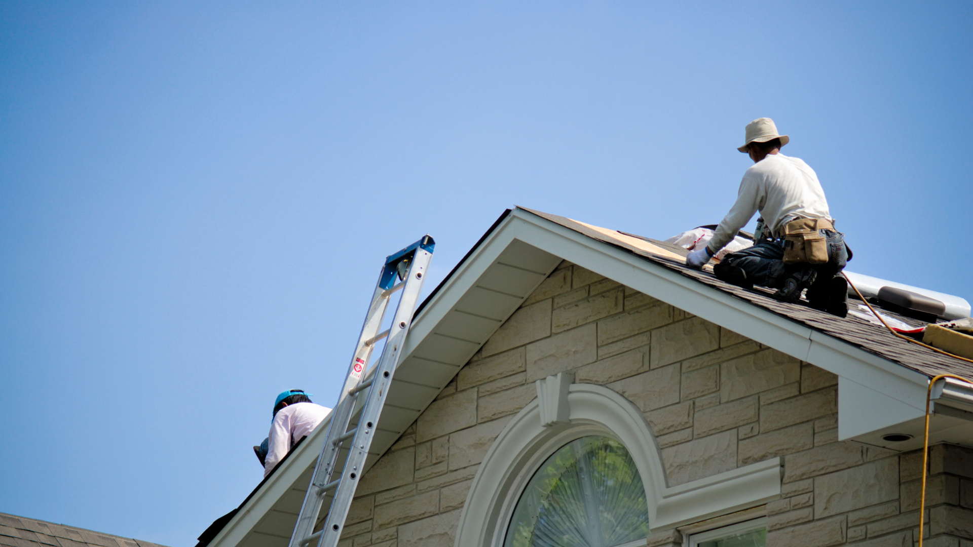 Roofers working safely on a sloped roof with a ladder, emphasizing ladder safety and proper equipment usage in roofing.