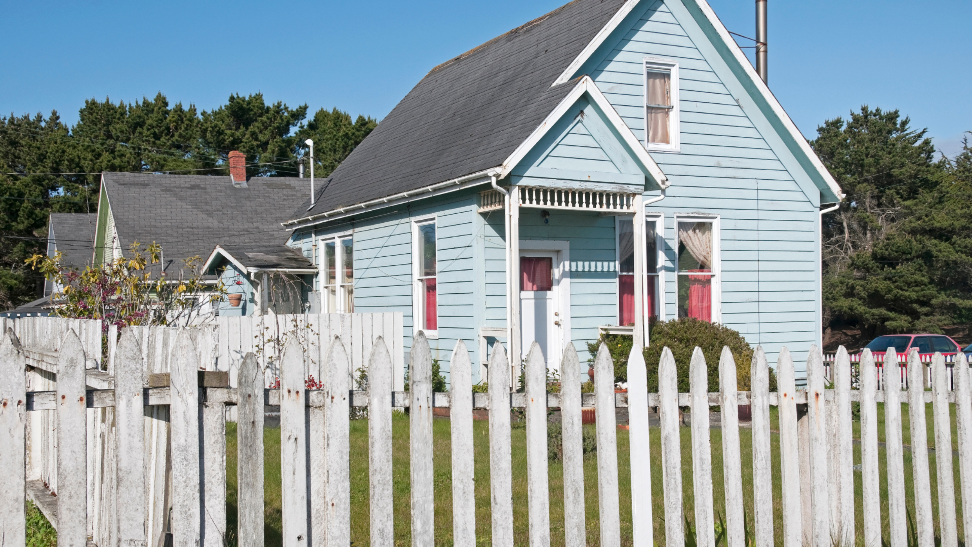 Blue house with white picket fence, surrounded by greenery, representing residential property aesthetics and security relevant to fencing companies in Minneapolis.