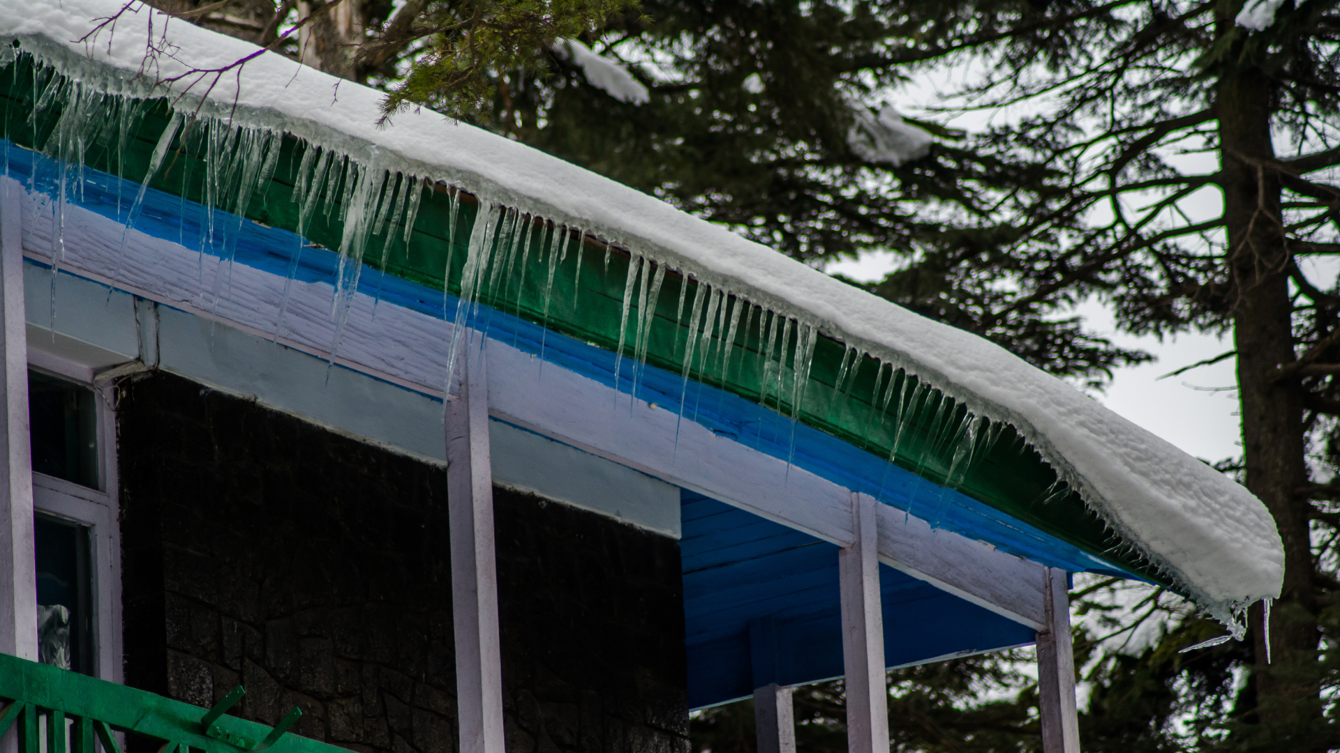 Icicles hanging from a snow-covered roof edge, illustrating potential ice dam formation and roof damage risks during winter.