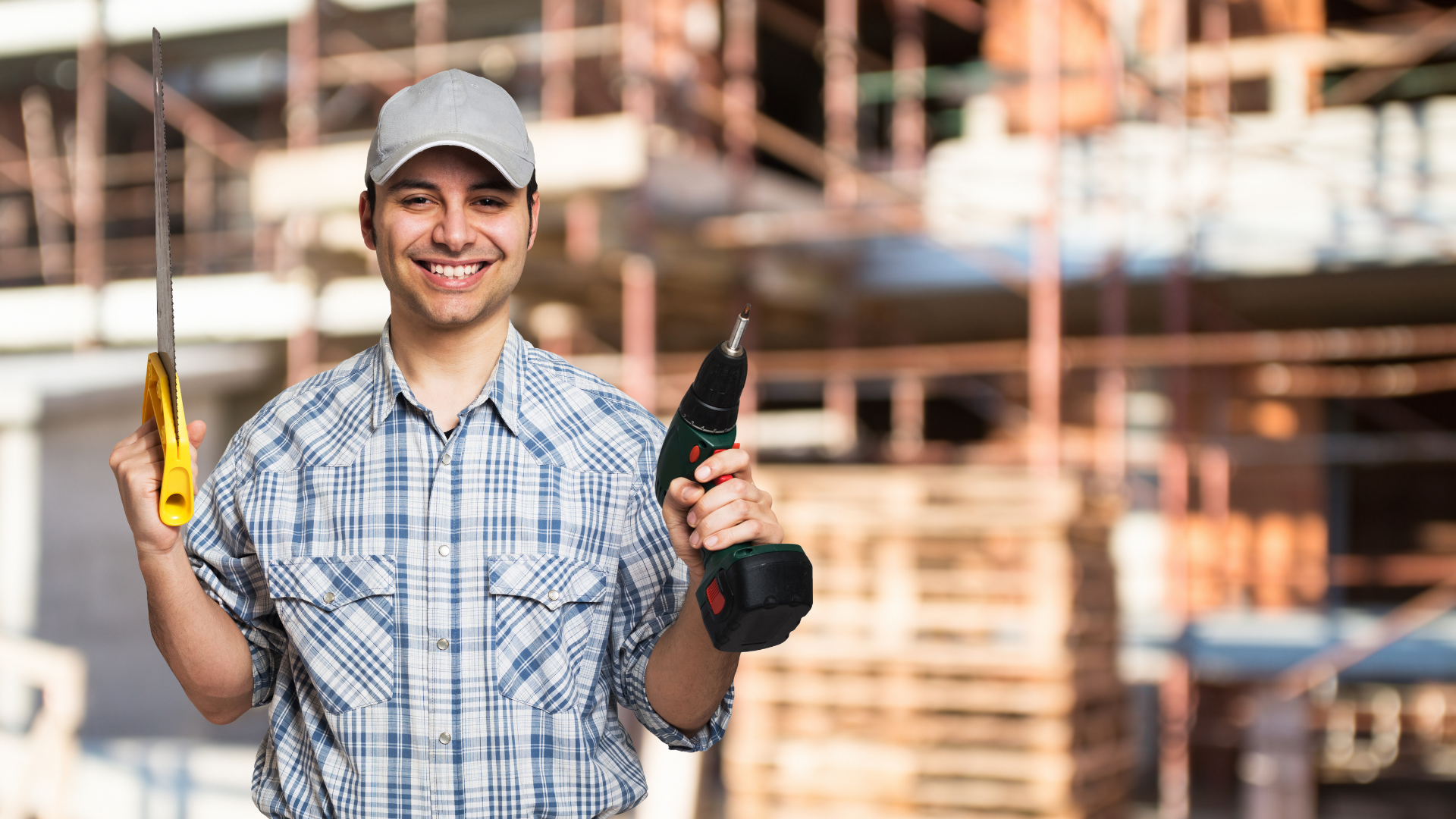 Smiling handyman holding a saw and cordless drill in front of a construction site, representing skilled home improvement services in Minneapolis.
