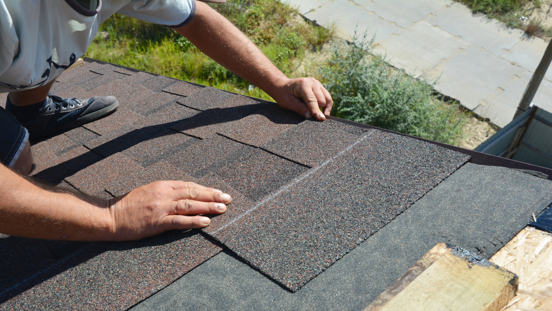 Person applying roofing shingles on a residential roof, demonstrating DIY repair techniques for managing roof leaks effectively.