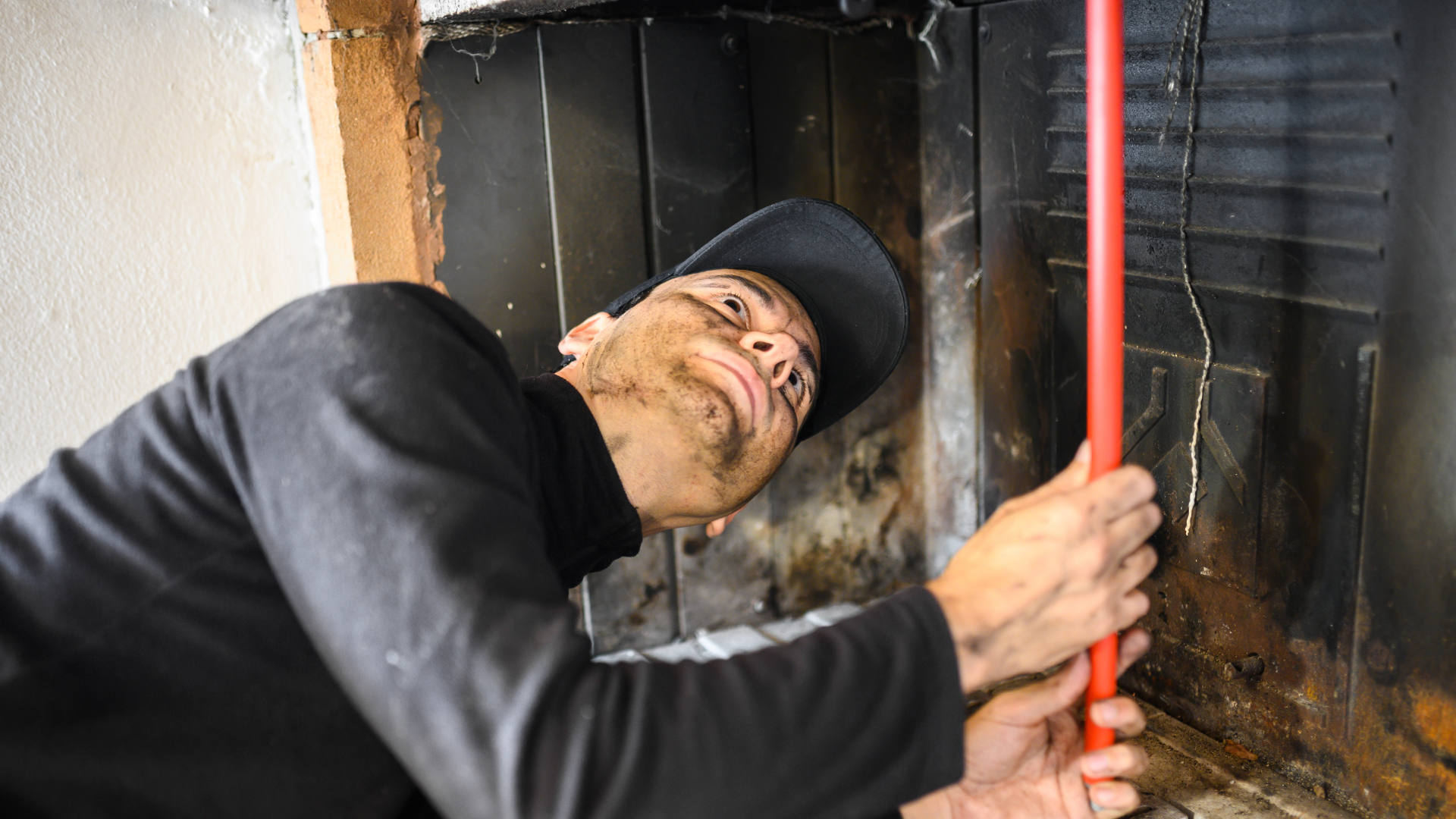 Chimney technician inspecting and cleaning fireplace with red tool, highlighting chimney maintenance services in Minneapolis.
