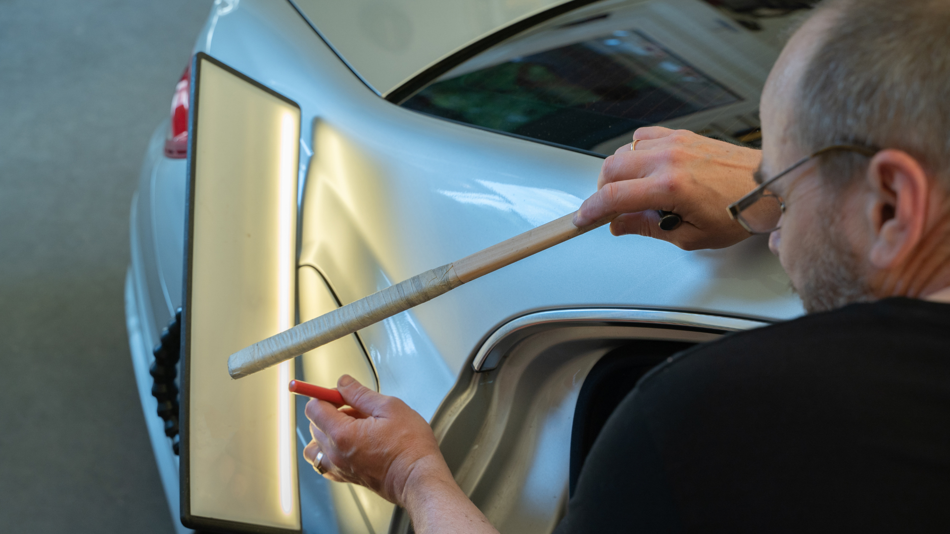 Technician using tools to repair car dents on a silver vehicle, demonstrating car dent restoration techniques relevant to Minneapolis car dent repair services.