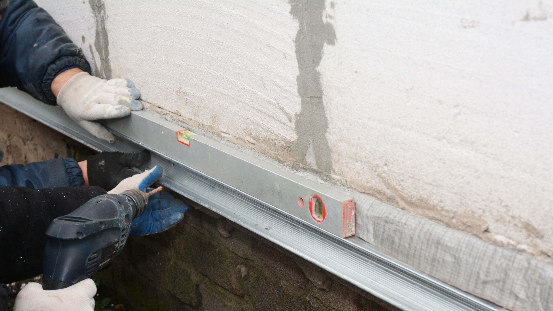 Workers using a level and drill to secure foundation repair materials, emphasizing the importance of stability in home foundations.