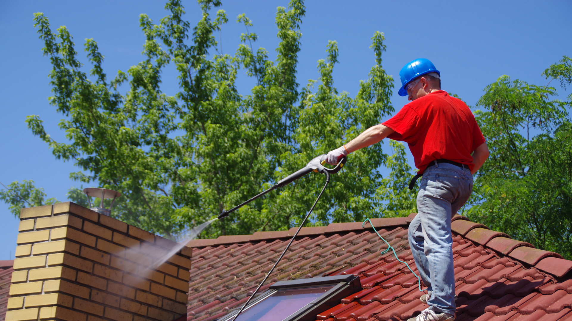 Man using a pressure washer to clean a roof, showcasing roof maintenance techniques for homeowners.