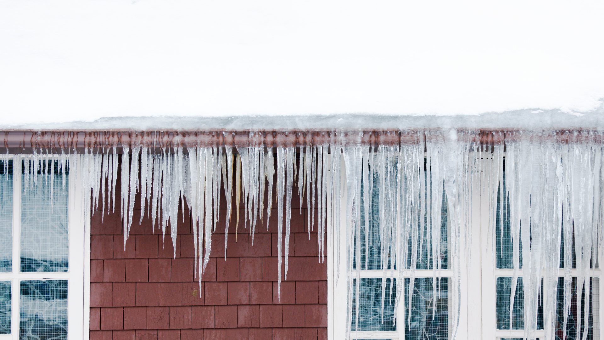 Icicles hanging from a roof over a red wooden wall, illustrating ice dam issues relevant to winter roofing challenges in Minneapolis, Minnesota.