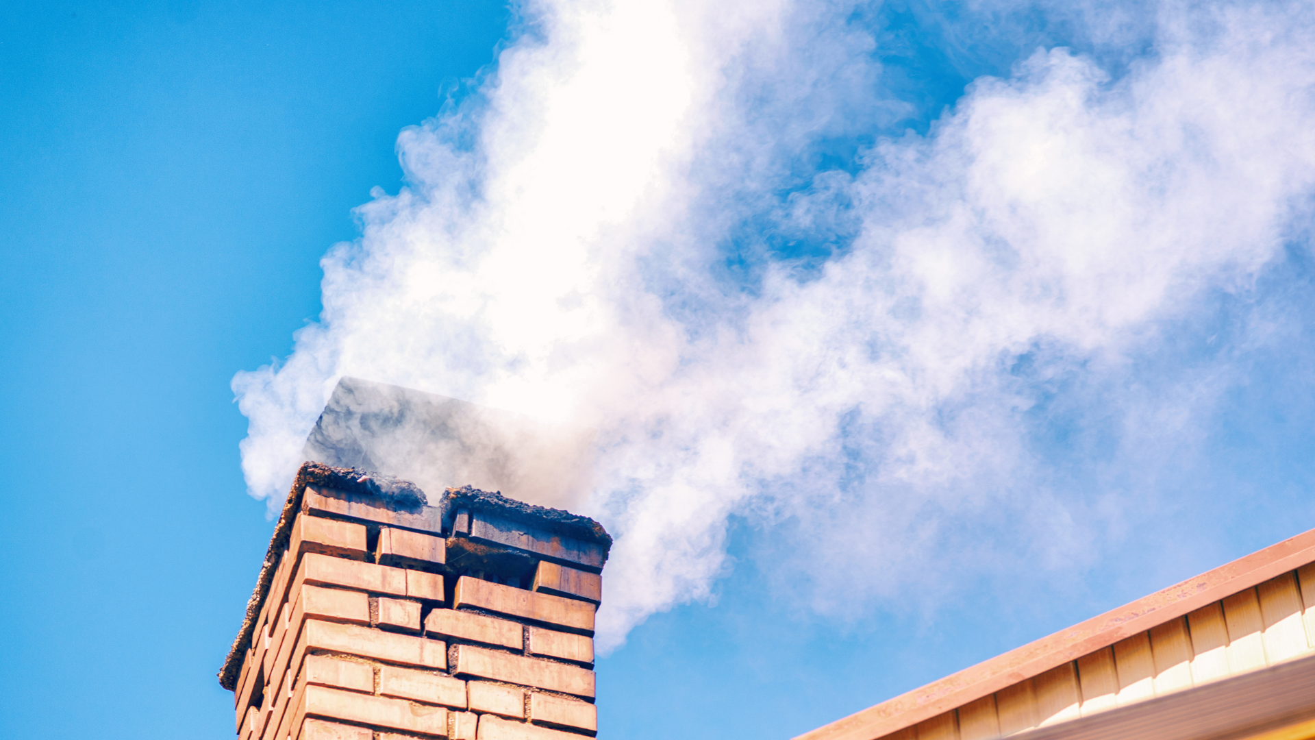 Chimney releasing smoke against a clear blue sky, illustrating proper fireplace function and maintenance in Minneapolis.