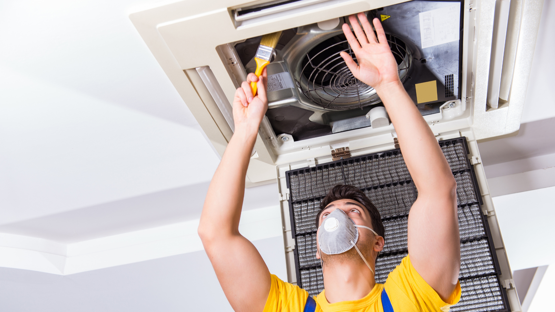 Technician performing maintenance on an HVAC unit, wearing a mask and using a brush to clean the filter, emphasizing the importance of regular HVAC service for energy efficiency.
