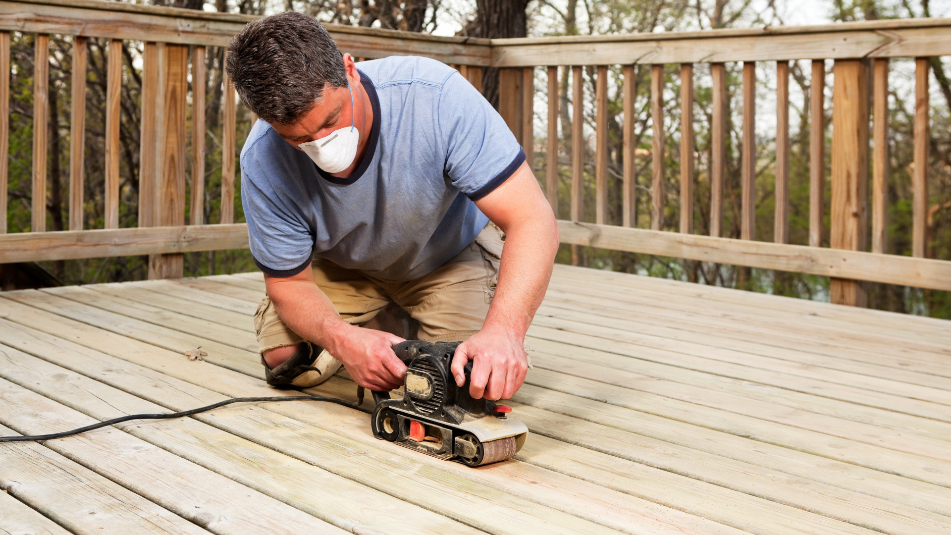 Man using a sander on a wooden deck, showcasing craftsmanship in deck construction for outdoor living spaces.