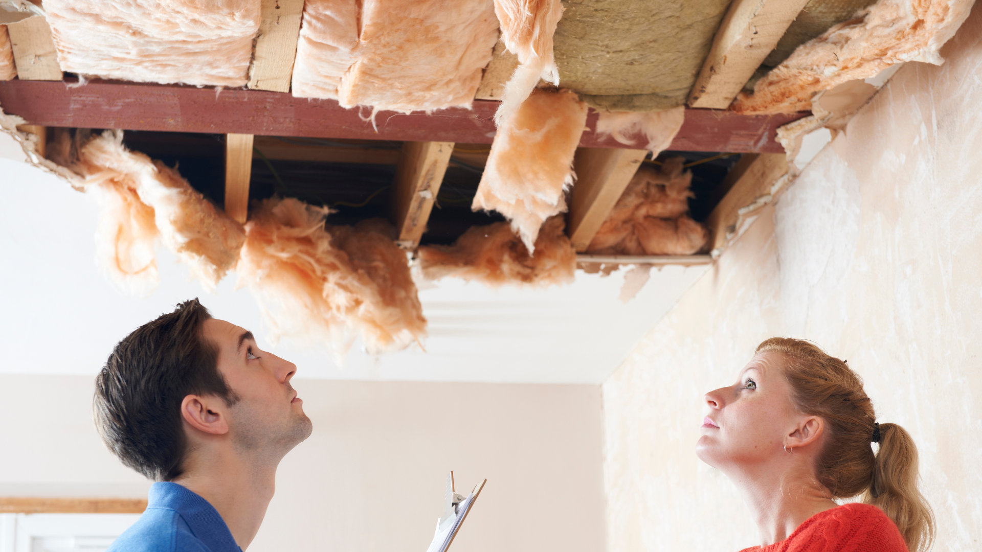 Man and woman inspecting damaged ceiling with exposed insulation, highlighting the importance of roof inspections in real estate transactions.