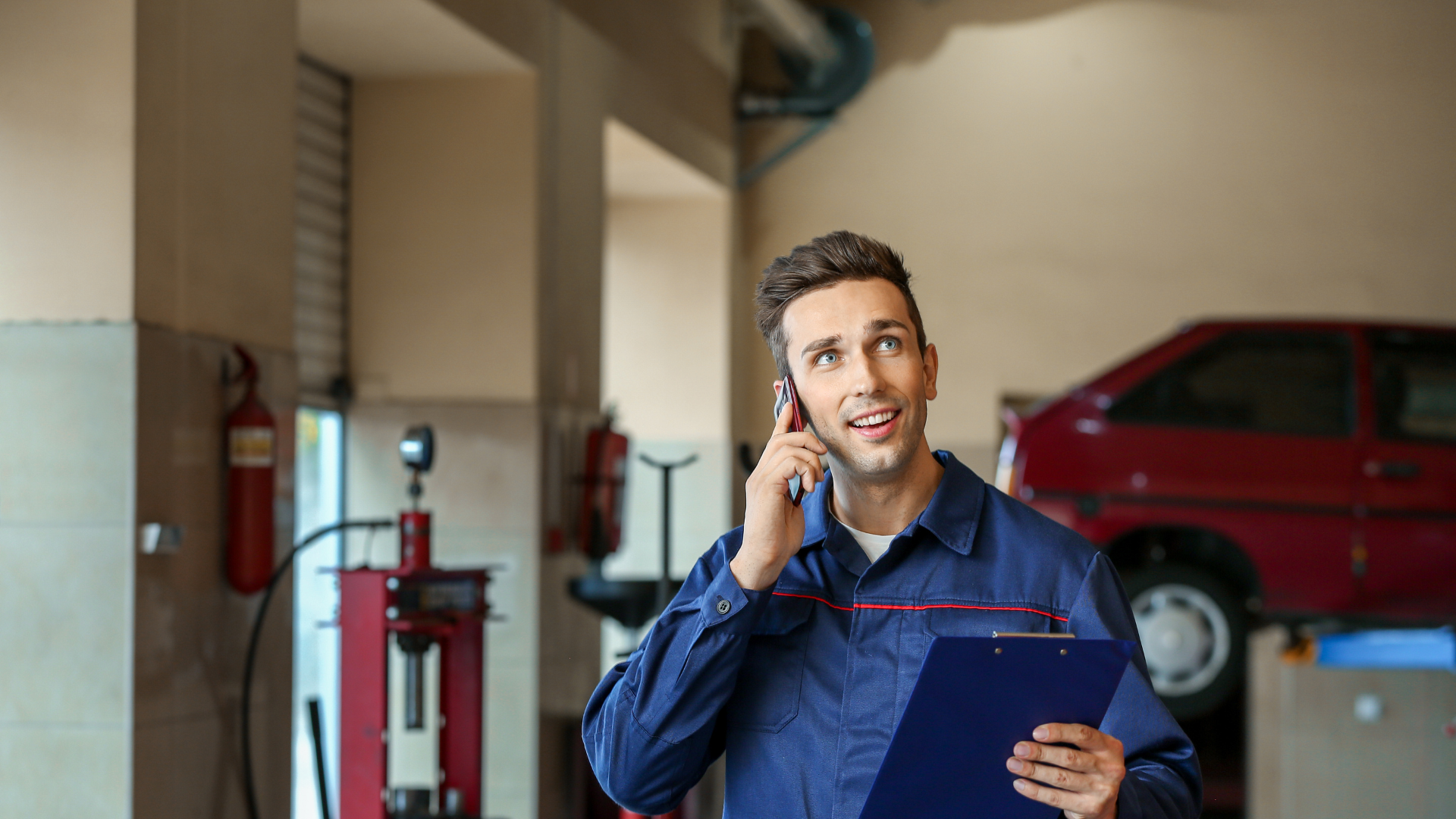 Car dent repair technician on phone, holding clipboard in auto repair shop, showcasing customer service and expertise in dent repair services.